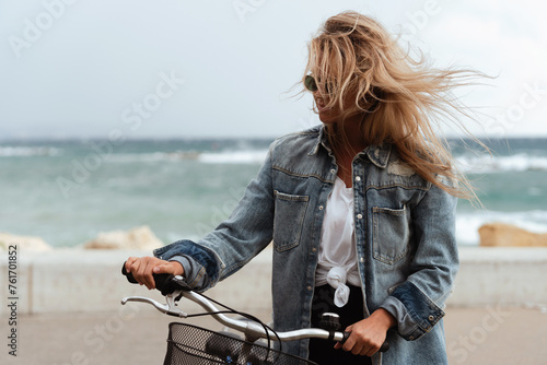 Woman in a denim jacket enjoys a solo bike ride along a seaside promenade
