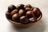 Roasted edible sweet chestnuts in bowl on light grey table, closeup