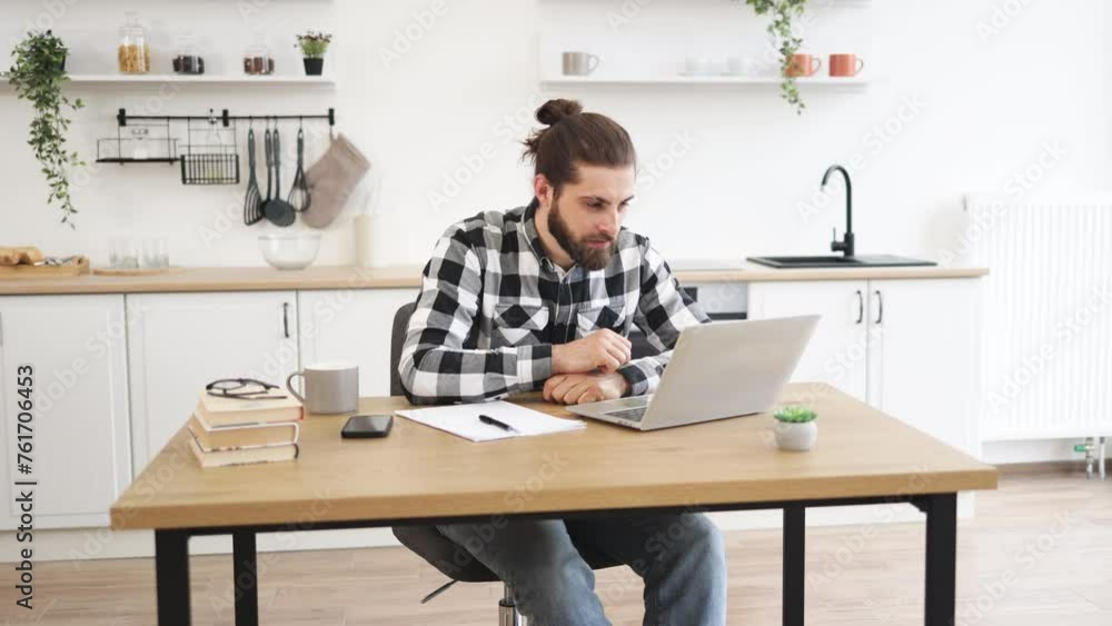 Excited Caucasian adult wearing checkered shirt and jeans raising hands up looking at laptop happy of good results of work. Emotional young businessman celebrating completion of great deal. Excited Caucasian adult wearing checkered shirt and jeans raising hands up looking at laptop happy of good results of work. Emotional young businessman celebrating completion of great deal.