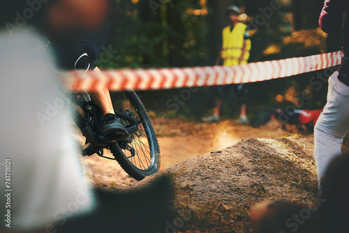 mountain bike drives through dusty berm at bike race. spectators cheering behind barrier tape. track marshal watches alertly. beautiful sunny weather in dark forest. selective focus on rear wheel photo