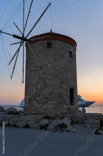Sunrise view of Mandraki windmills in Rhodes town harbor by the sea and a cruise ship