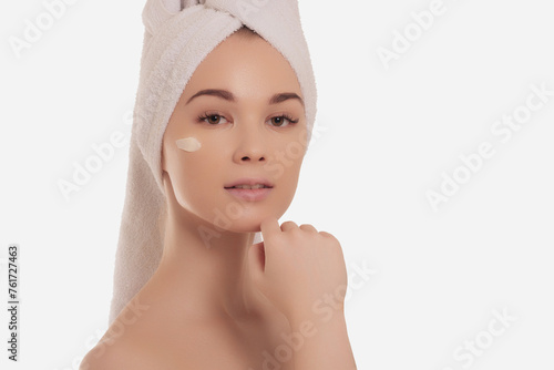 Beautiful young woman applying cream in bathroom, pretty lady wrap towel on head put facial moisturizer lifting hydrating moisturizing creme, skin care treatment concept