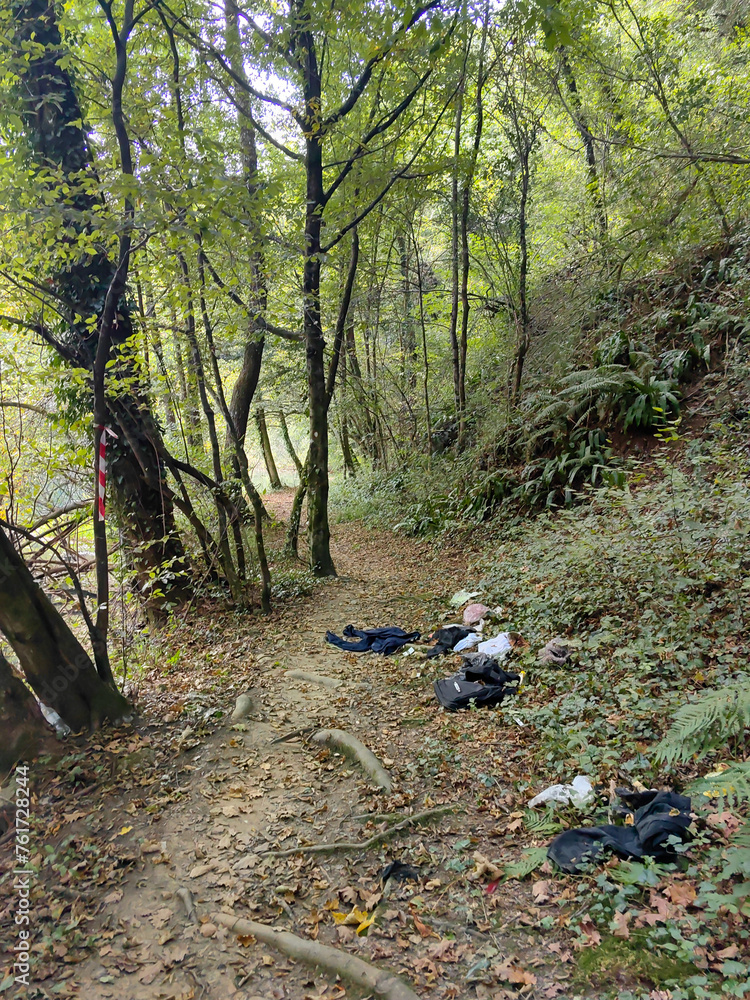 Abandoned clothes of refugees on the forest trail by the blue and green river Slunjcica passing through the woods and the treeline by the river edge Abandoned clothes of refugees on the forest trail by the blue and green river Slunjcica passing through the woods and the treeline by the river edge