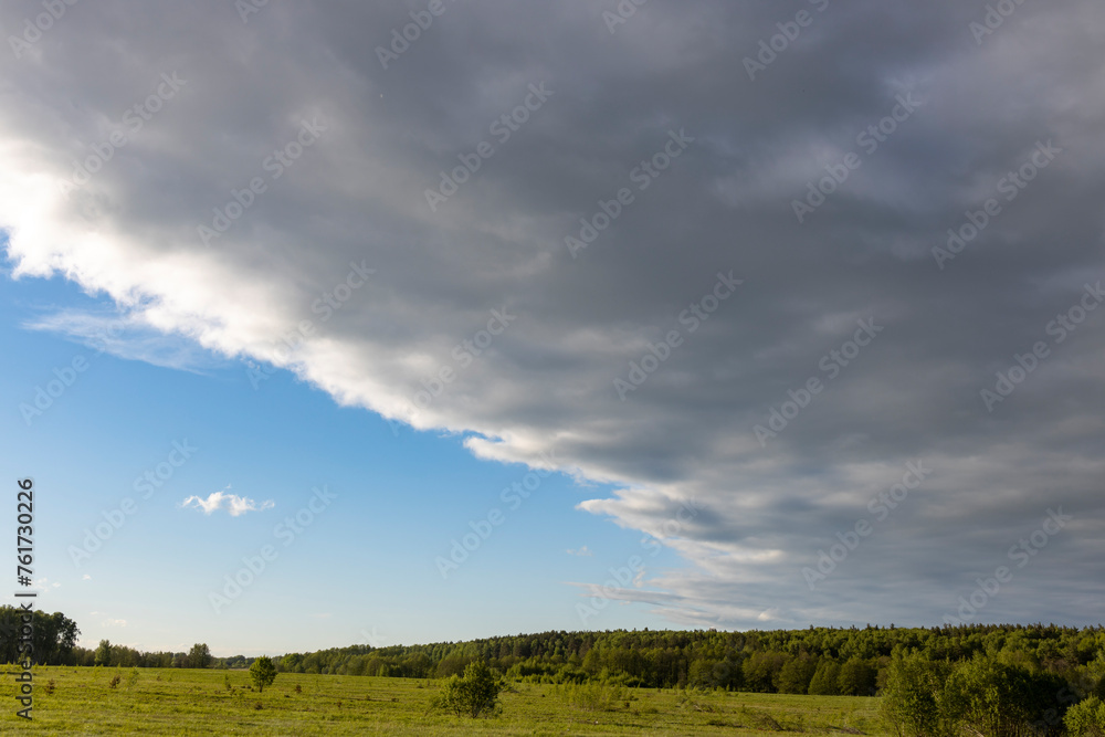 Sunny landscape against a dramatic sky, countryside in early spring, young green grass in a field Sunny landscape against a dramatic sky, countryside in early spring, young green grass in a field