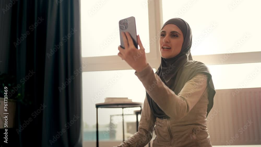 Pretty Arab woman in hijab having video call on smartphone, smiling to friend Pretty Arab woman in hijab having video call on smartphone, smiling to friend