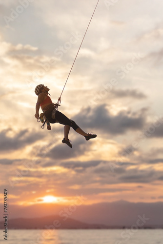 A woman is hanging from a rope in the air. The sky is cloudy and the sun is setting
