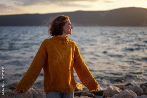 Smiling young woman in a yellow sweater looking at view at sunset enjoy sunshine.