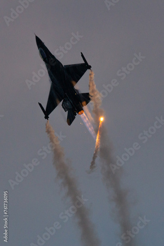 A Belgian Air Force F-16 pulls up sharply with its afterburner on while firing a flare during an evening airshow display.