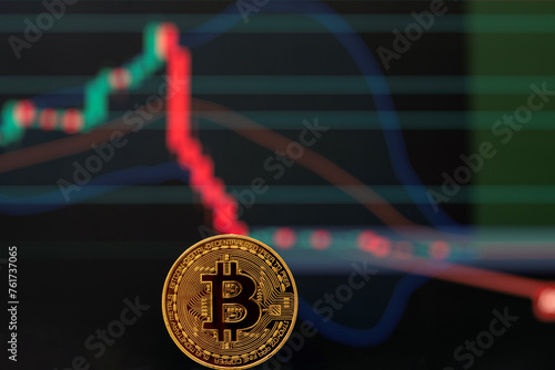Bitcoin gold coin and defocused downward graph in dark background.