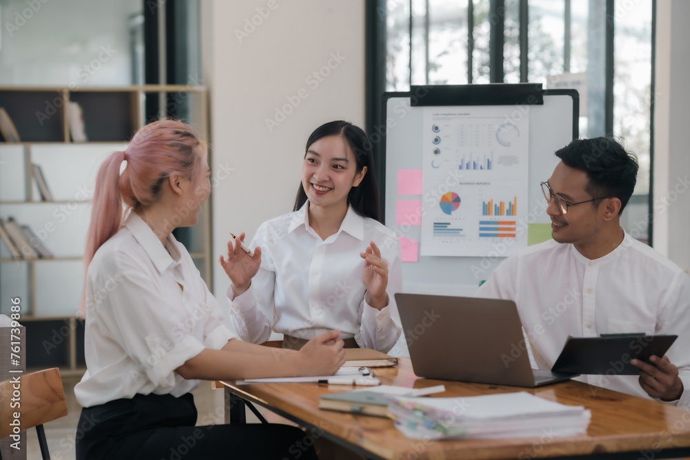 Fototapeta premium Three people are sitting around a table with a white board behind them. They are smiling and talking to each other