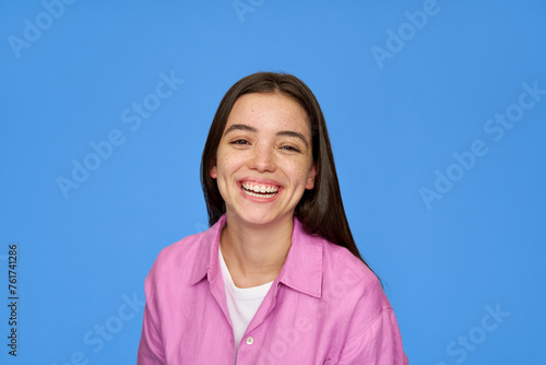 Smiling pretty freckled gen z brunette Latin girl, cute happy Hispanic teen student wearing pink shirt looking at camera laughing standing isolated on blue background. Close up portrait.