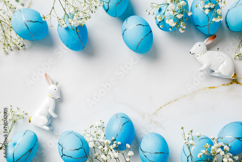 Happy Easter background with blue eggs, rabbits, spring flowers on stone table. Flat lay, top view, copy space.
