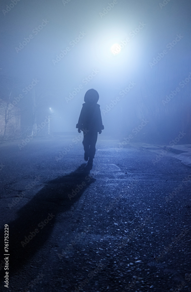 The silhouette of a little girl walking down a misty street.