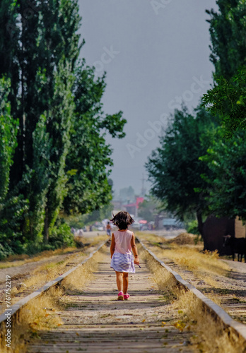 A little girl in a summer dress walking amidst an abandoned railway.