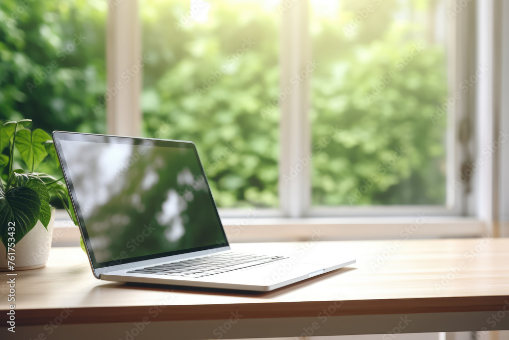 Modern laptop on wooden desk in sunny room with green view Modern laptop on wooden desk in sunny room with green view