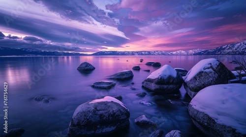 A stunning sunset illuminates a lake with snow-covered rocks in the foreground  creating a striking winter scene.