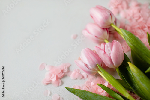 A bouquet of pink tulips and pink confetti on a white background in the lower right corner. Copy space. Top view. 