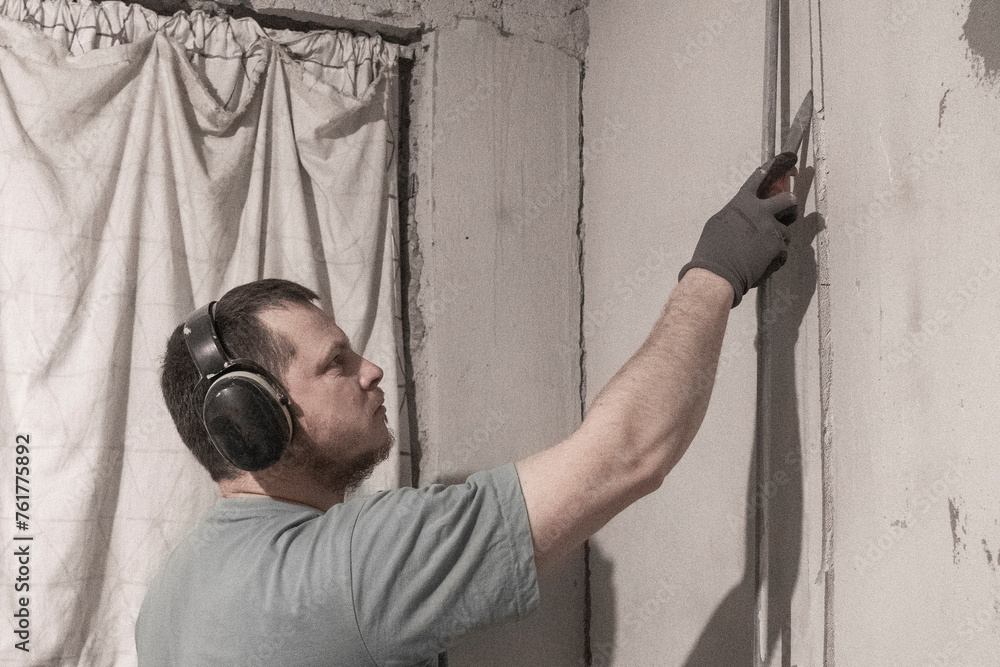 Man Uses Chisel to Extract Material from Cut Hole for Electricity Installation. Man Uses Chisel to Extract Material from Cut Hole for Electricity Installation.