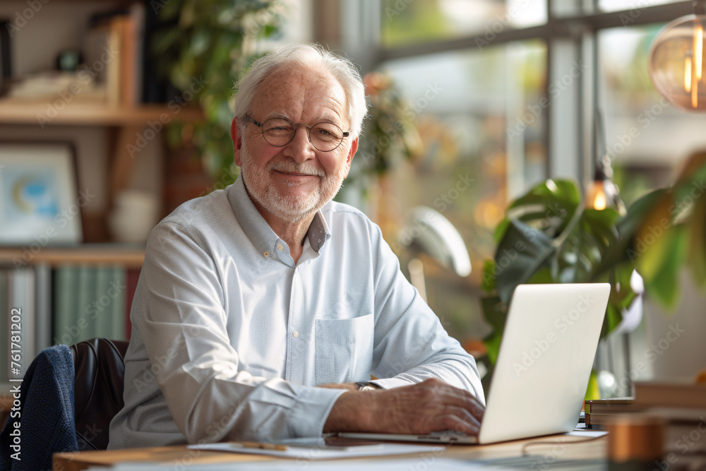 Smiling elderly man with white hair at laptop in a sunny office Smiling elderly man with white hair at laptop in a sunny office