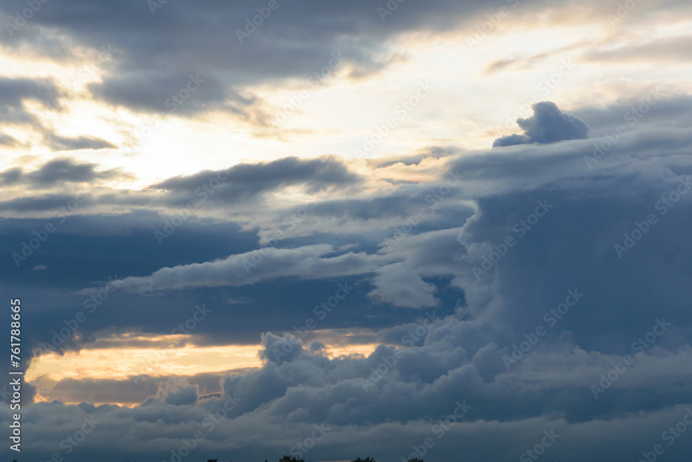 Very large lush clouds in a dramatic sky, the beginning of rain, blinding sunlight visible through the gaps in the clouds