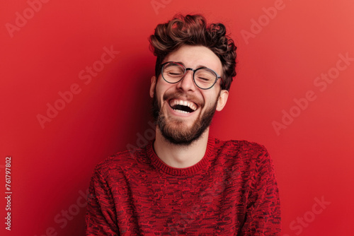 Man laughing with closed eyes on red background - A bearded man in a red sweater stands out brightly against a red background, laughing heartily with his eyes gently closed