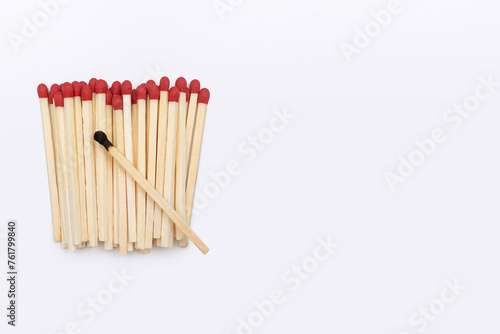 A set of matches and one burnt match on them on a white background with space for text. Close-up of red matches without a matchbox and one burnt match in the center.