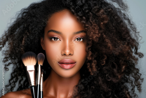 A stunning beauty portrait of a woman with luscious curly hair holding makeup brushes near her face photo
