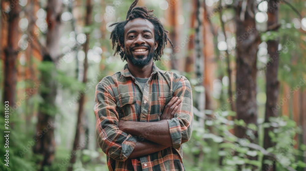 Cheerful man with dreadlocks smiles broadly while posing with arms crossed in a lush green forest setting, radiating positivity Cheerful man with dreadlocks smiles broadly while posing with arms crossed in a lush green forest setting, radiating positivity