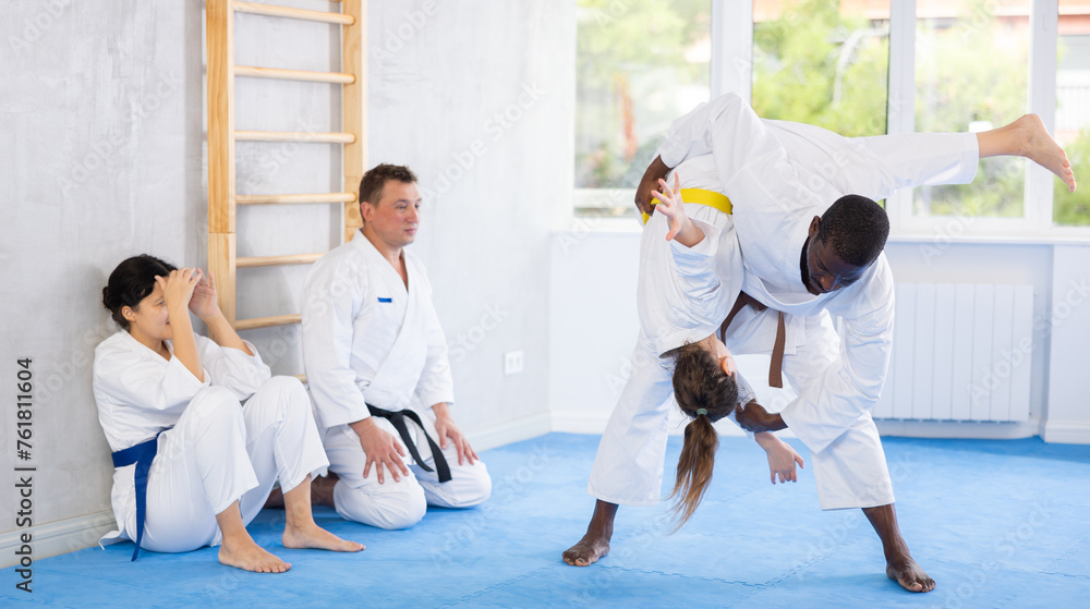 Adult man and adult woman judokas practicing judo technique in group in gym