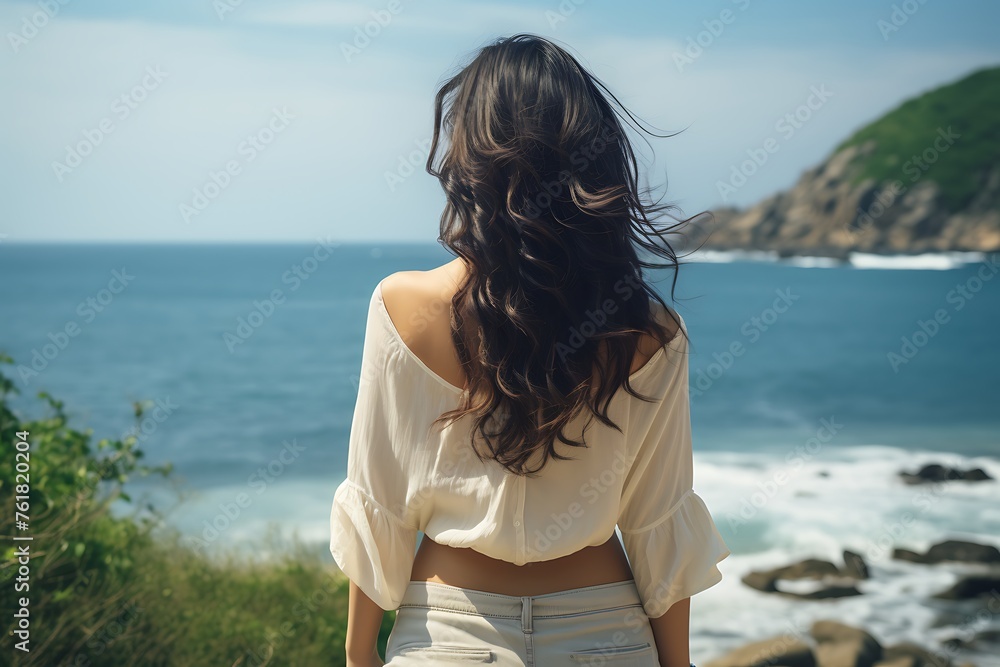 Back view of young brunette woman in standing on seashore