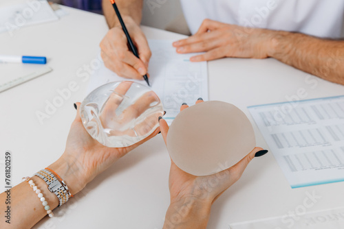 A woman chooses plastic breast implants at a doctor's consultation. The girl is holding silicone breasts in her hands choosing and comparing photo