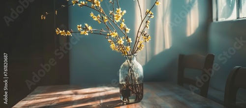 Shrub branch with yellow flowers in a glass vase on a table in a room. photo