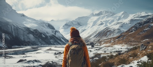 A traveler with a backpack admires the snowy mountain peak under a clear sky, surrounded by a stunning natural landscape of hills and mountain ranges