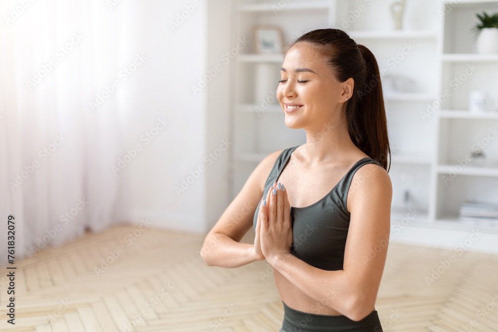Serene asian female meditating with closed eyes and making namaste gesture