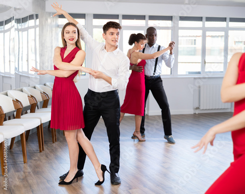 Young girl with multinational group of active people dancing couple enjoying active swing during dance party in modern ballroom