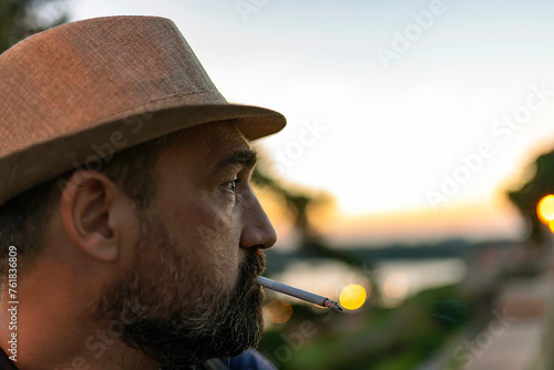 Handsome Mature Man with Beard and Hat Smoking a Cigarette During a Sunset in the City © Jelena