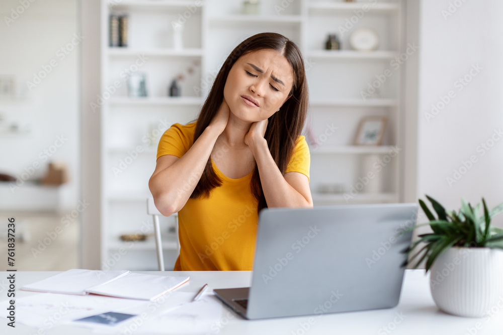 Asian woman feeling pain in neck, having strain while working at laptop Asian woman feeling pain in neck, having strain while working at laptop
