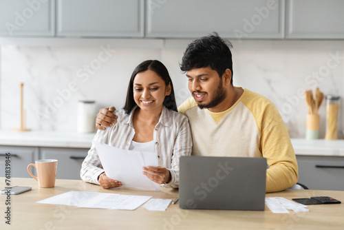 Happy young indian spouses reading letter from bank, kitchen interior
