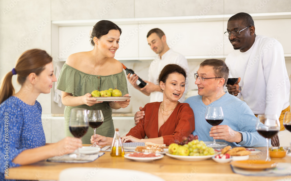 Multicultural female and male friends chatting and drinking wine at table