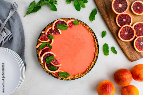Blood Orange Cheesecake Tart on a White Marble Table: Raspberry orange curd cheesecake tart garnished with mint leaves in graham cracker crust