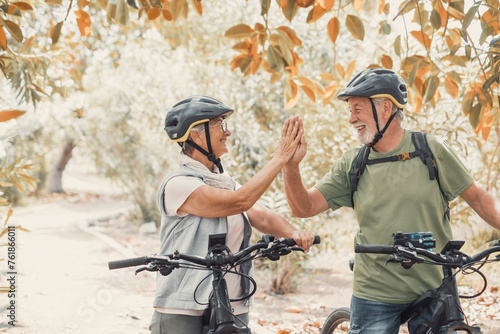 Couple of two seniors giving five together outdoors having fun with bicycles enjoying nature. Couple of old people building a healthy and fit lifestyle..
