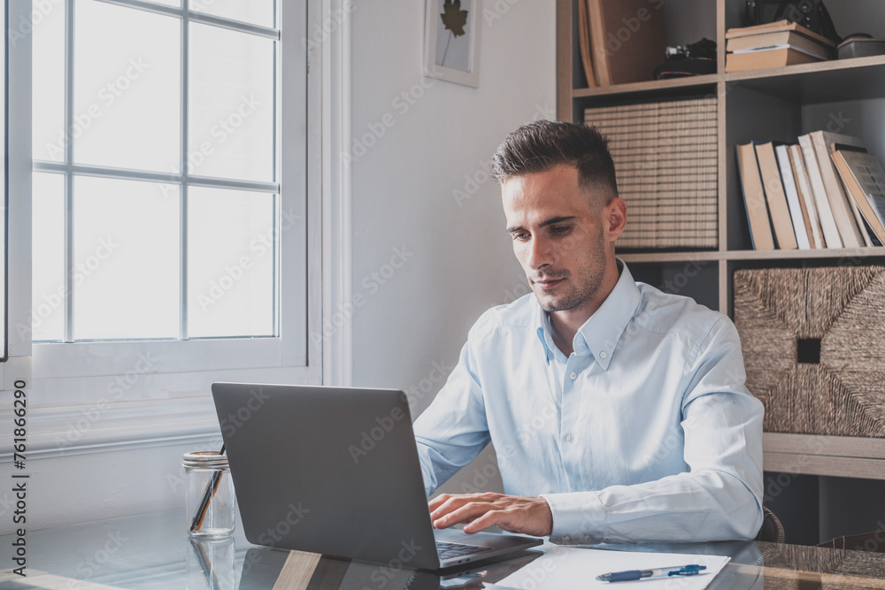 Happy young caucasian millennial businessman working at home at desk with laptop or computer having fun. Young male person in video conference taking care of the business or market.. Happy young caucasian millennial businessman working at home at desk with laptop or computer having fun. Young male person in video conference taking care of the business or market..