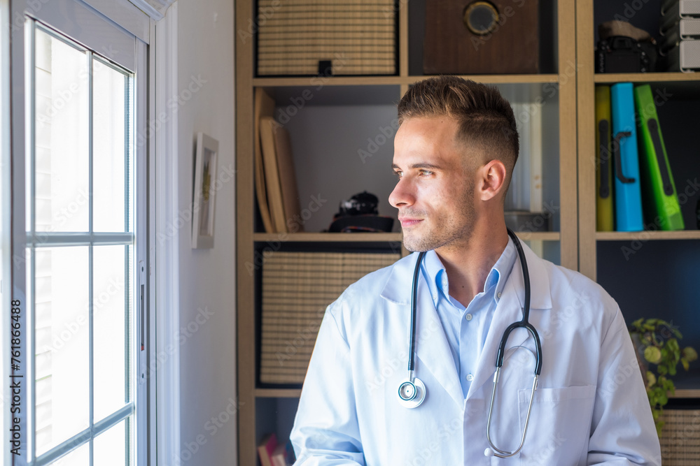 Pensive young male caucasian doctor in white medical uniform look in window distance thinking or pondering, serious man GP plan future career or success in medicine, visualize at workplace writing. Pensive young male caucasian doctor in white medical uniform look in window distance thinking or pondering, serious man GP plan future career or success in medicine, visualize at workplace writing.