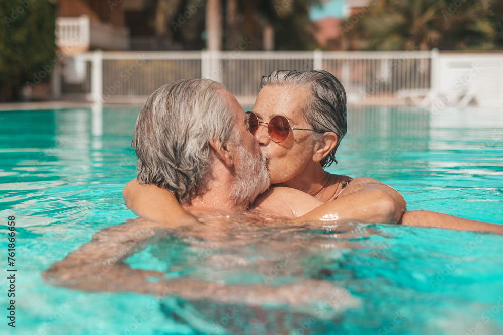 Couple of two happy seniors having fun and enjoying together in the swimming pool smiling and playing. Happy people enjoying summer outdoor in the water.
