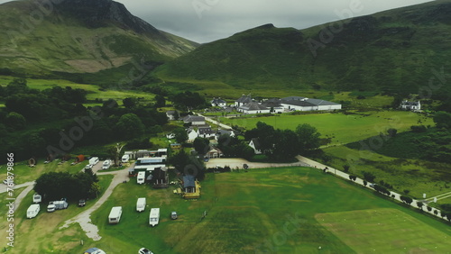 Scottish village aerial view: road, cottages, houses, distillery, camping in green valley at summer cloudy day. Picturesque mountains scenery from Arran Island, Scotland. Footage cinematic shot