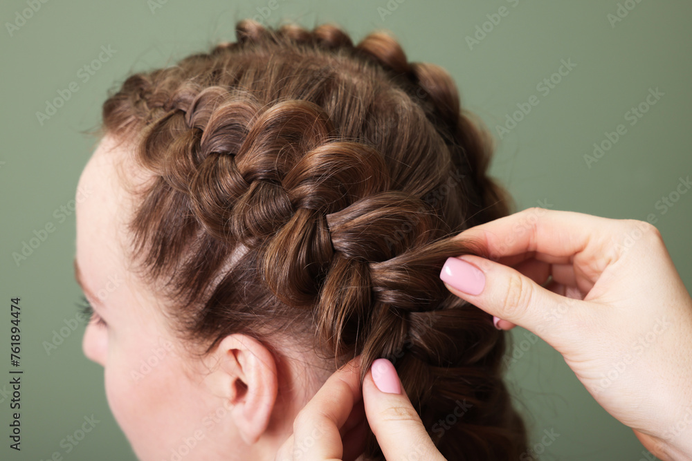 Fototapeta premium Professional stylist braiding woman's hair on olive background, closeup