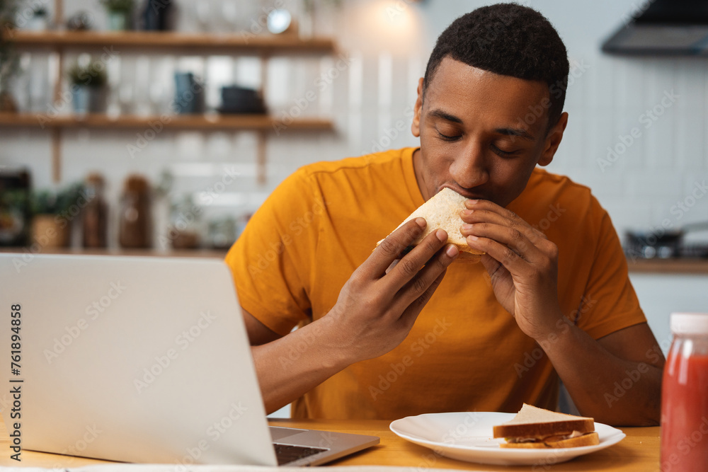 Portrait of attractive African American man holding tasty sandwich eating, enjoying with closed eyes Portrait of attractive African American man holding tasty sandwich eating, enjoying with closed eyes