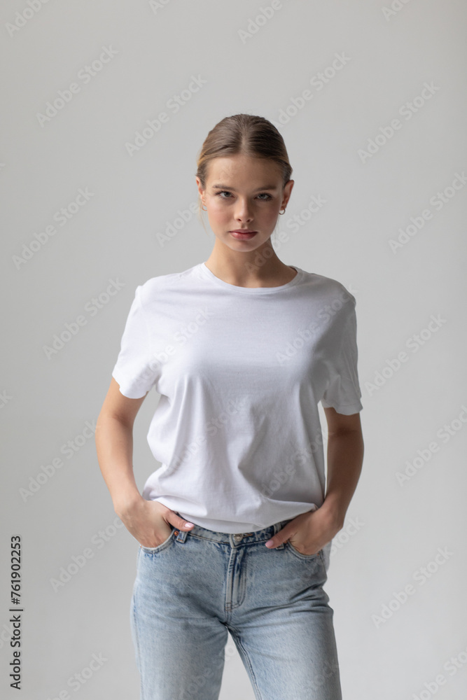 Beautiful blonde woman in a white T-shirt and blue jeans posing on a white background