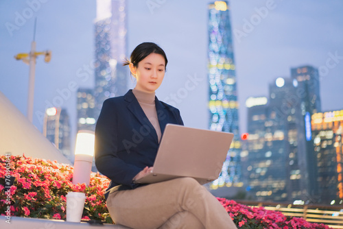 Young Businesswoman Working on Laptop in Evening Cityscape