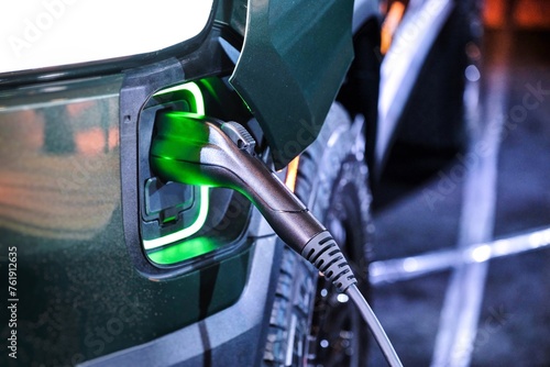 Close up of electric vehicle EV truck van charging on charging station with green power light reflecting on the handle.